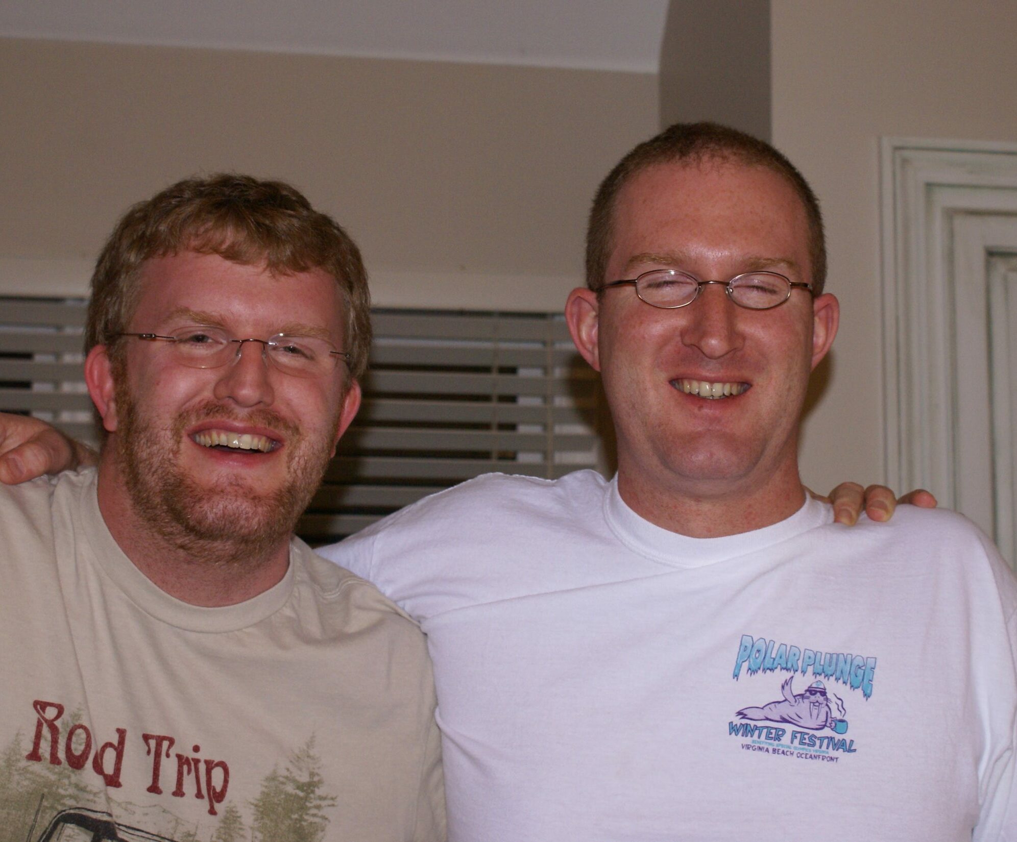 About - two smiling men with glasses engaged in a professional development seminar, one wearing a gray "road trip" t-shirt and the other in a white "polar plunge winter festival" t-shirt, standing indoors