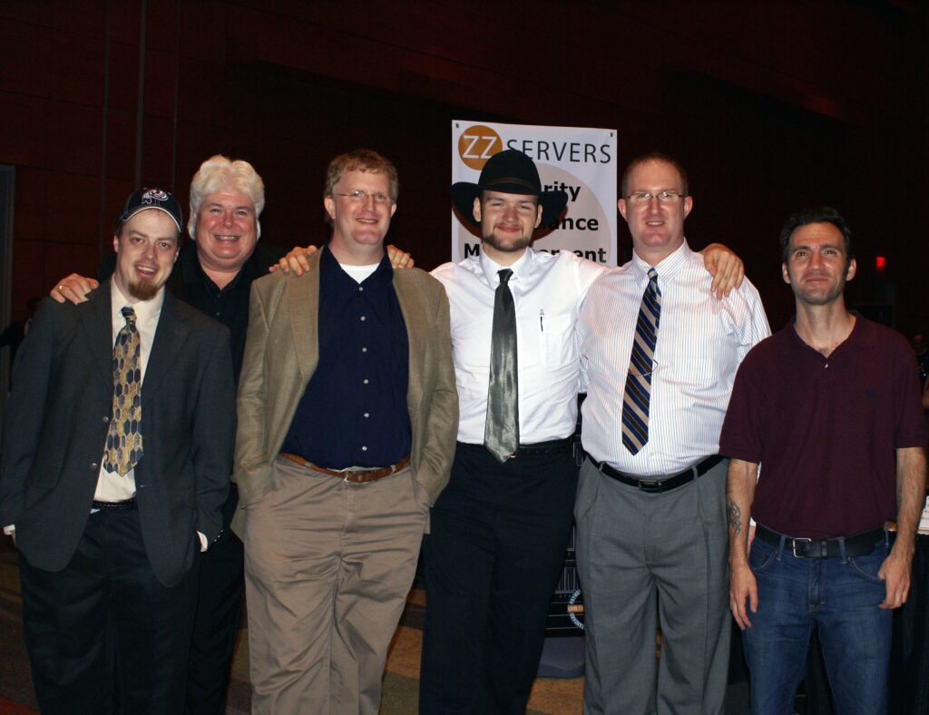 Group of six men posing with smiles at a cybersecurity conference, standing in front of a "zzcervers security conference" banner.