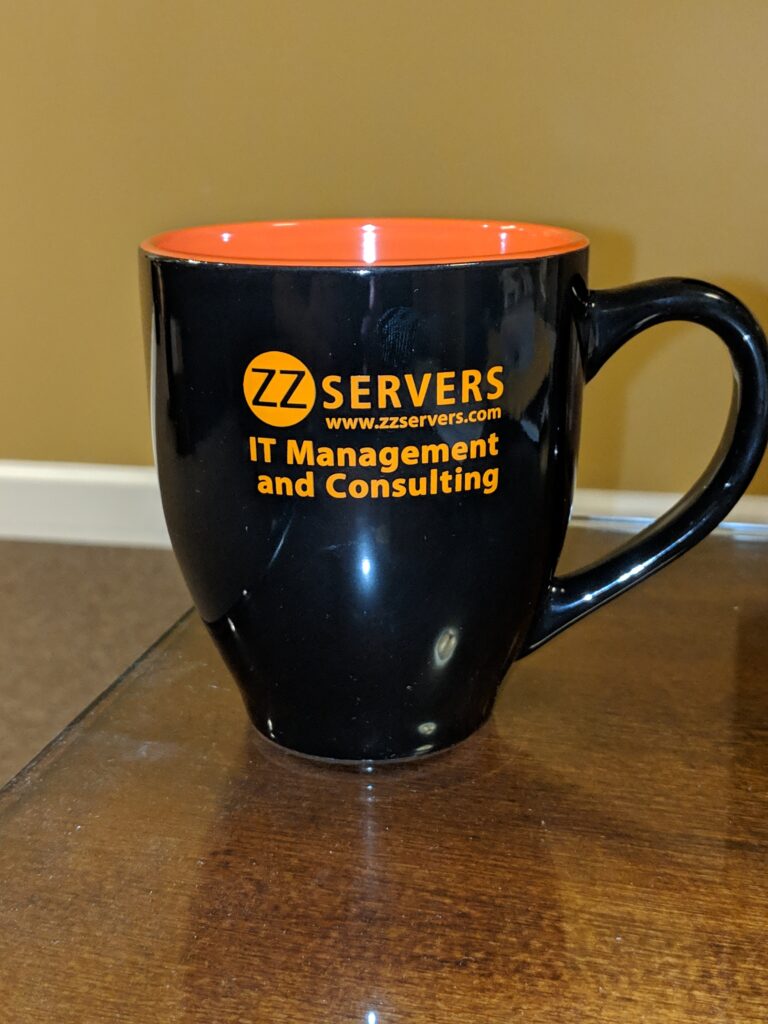 Black mug with orange interior featuring "zz servers - it management and consulting" logo on a wooden surface.