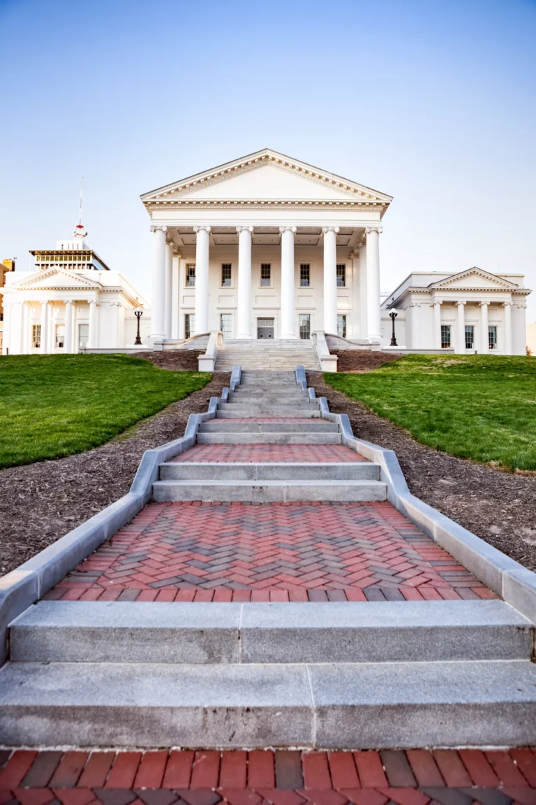 Stone steps leading up to a grand white building with columns and pediment, flanked by two smaller structures housing it services under a clear sky.