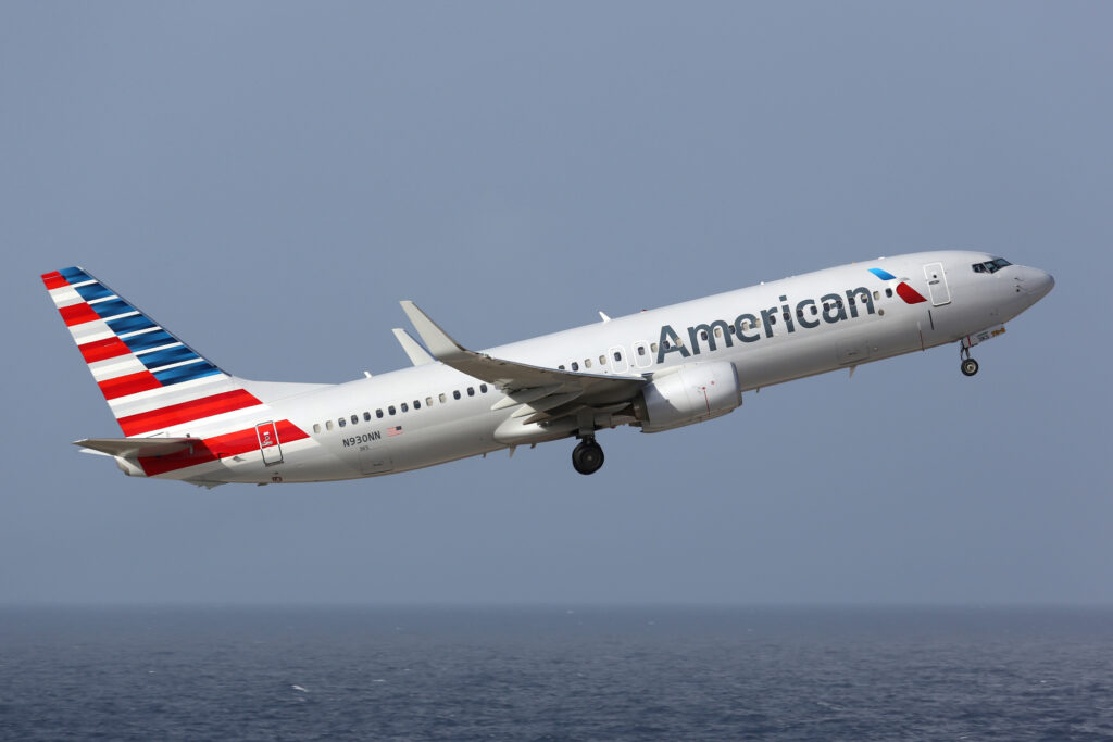 An American Airlines plane triumphantly flying over the ocean.