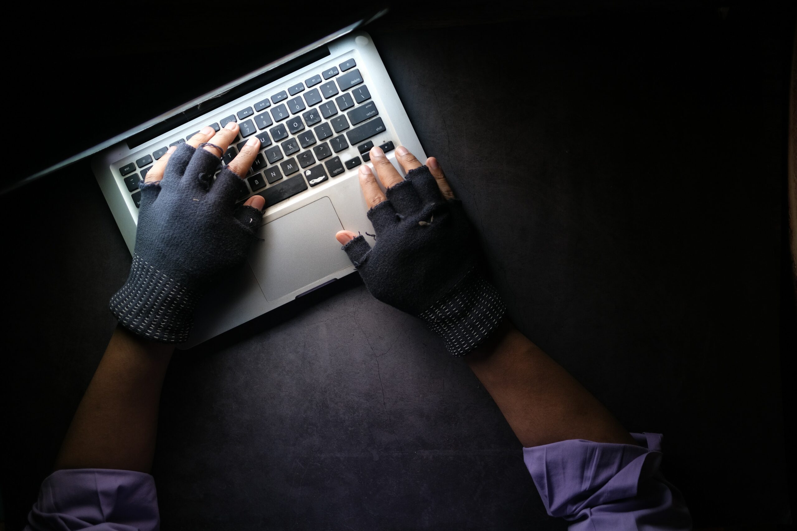 A person is typing on a laptop with gloves on, ensuring the security of their confidential information.