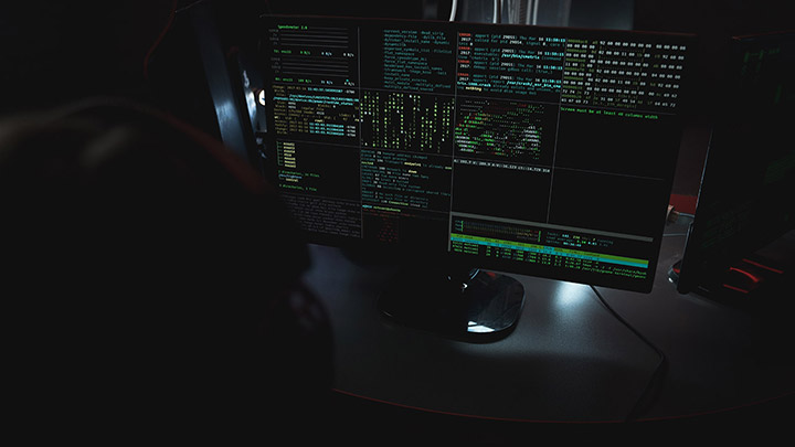 A person surveilling cmc threat intelligence from a computer screen in the dark
