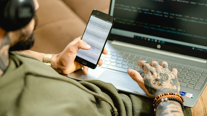 A man with tattoos conducting Cyber Threat Intelligence using a laptop and cell phone