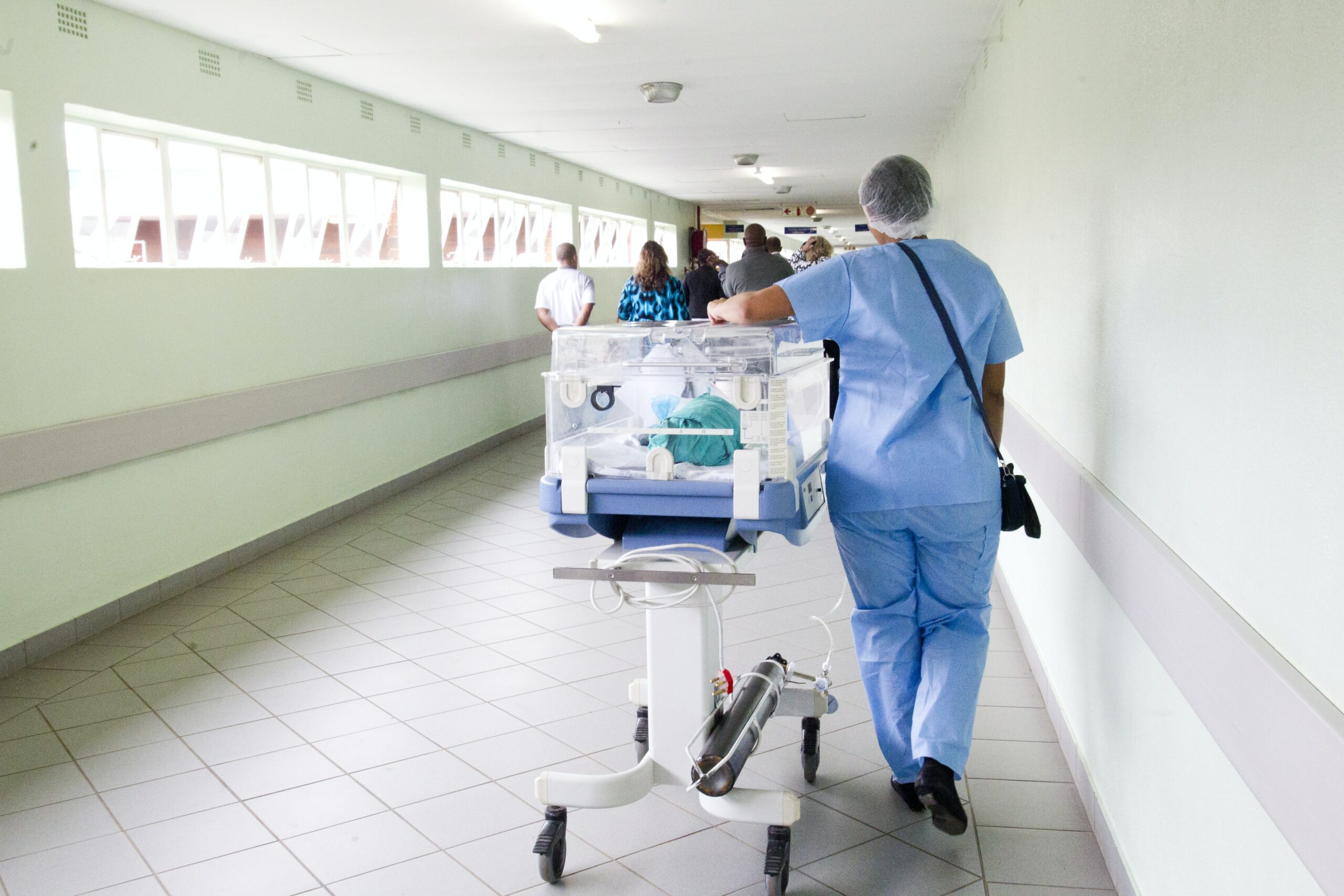 A nurse is walking down a hallway in a hospital with a baby on a cart.