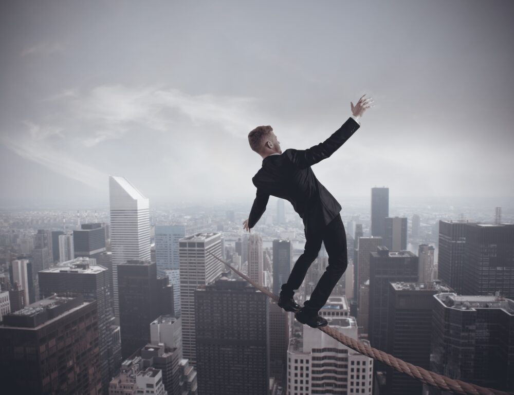 A businessman performing a risky balancing act over a city represents the challenges faced in implementing a Third-Party Risk Management Program.